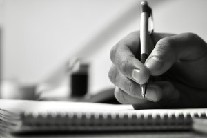 Une main tient un stylo, au-dessus d'un cahier et s'apprête àécrire